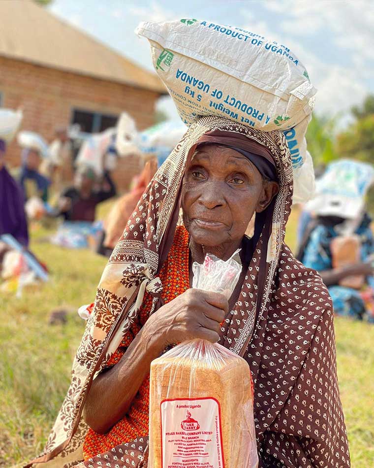 Elderly-seated-on-ground-with-a-bag-of-maize-floor-balancing-on-the-head-after-recieving-food-aid-in-Eastern-Uganda